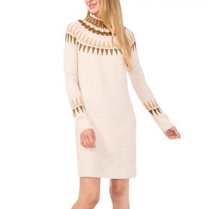 A cream-colored sweater dress with a high neckline, featuring a brown geometric pattern across the chest, shoulders, and cuffs. The dress is long-sleeved and knee-length, offering a cozy, stylish look.