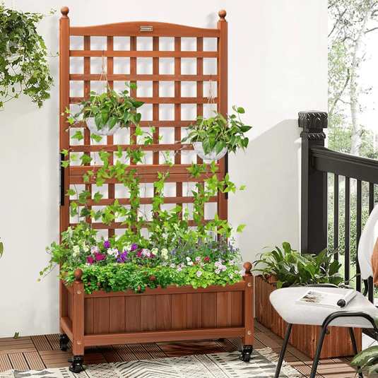 A wooden planter box with an attached trellis supports climbing plants, with hanging pots and flowers below, placed on a balcony with additional decor.