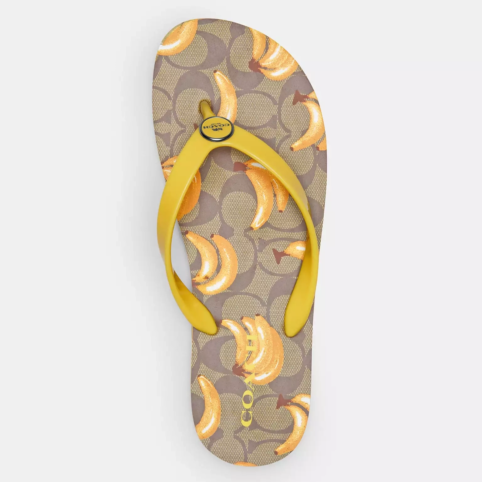 A single sandal with a fruit print featuring sliced bananas on a patterned background, with a yellow thong strap bearing the Coach brand logo.