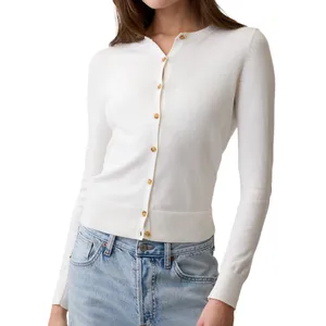 A woman is wearing a white long-sleeve cardigan with gold buttons over a pair of light blue jeans.