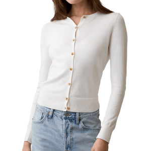 A woman is wearing a white long-sleeve cardigan with gold buttons over a pair of light blue jeans.