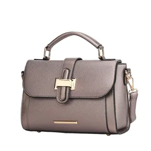 A taupe leather handbag with a top handle, gold-tone hardware, a flap closure with a decorative buckle, and an optional shoulder strap.