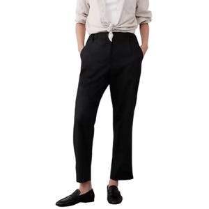A person is wearing black tailored trousers paired with a light-colored shirt tied at the waist, and black loafers.