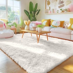 A cozy living room features a soft, white, fluffy rug, a wooden coffee table with plants and books, a pink couch adorned with colorful pillows, and a large potted plant by a bright window.