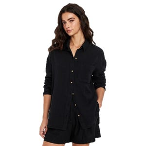 A woman is wearing a long-sleeve black button-up shirt with a collar and a chest pocket, paired with black shorts.