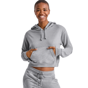 A woman wearing a gray Hanes Women's French Terry Cropped Hoodie. The hoodie features a drawstring hood, kangaroo pocket, and is paired with matching drawstring lounge pants, creating a cozy and casual look.