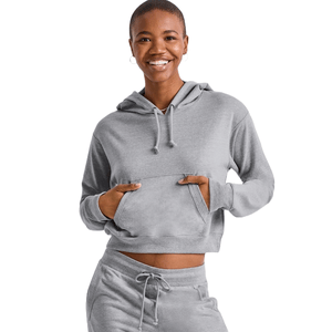 A woman wearing a gray Hanes Women's French Terry Cropped Hoodie. The hoodie features a drawstring hood, kangaroo pocket, and is paired with matching drawstring lounge pants, creating a cozy and casual look.