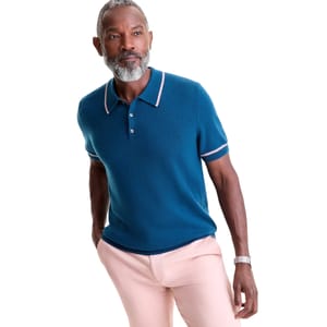A man wears a blue short-sleeved polo shirt with pink trim and light pink pants.