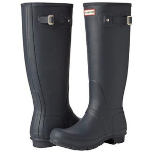Hunter Original Tall Boots are knee-high, waterproof, black rubber boots with an adjustable strap and silver buckle near the top. They feature a textured sole for traction and the Hunter logo at the front.