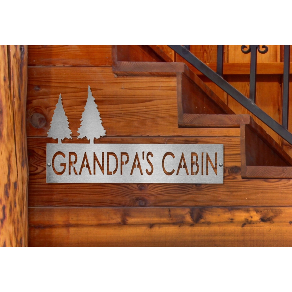 A custom steel sign mounted on wooden stairs, reading \“GRANDPA'S CABIN\“ with two tree silhouettes beside the text, reflecting a rustic cabin theme.