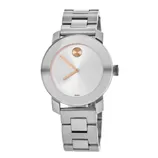 A stainless steel watch with a minimalist design features a round white dial, gold-toned hands, and a single dot marker at 12 o'clock. The bracelet has a polished metal finish.