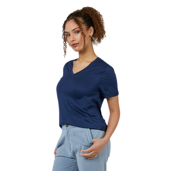 A person is wearing a navy V-neck t-shirt, light blue jeans, and blue slip-on shoes with white soles, standing against a gray background.