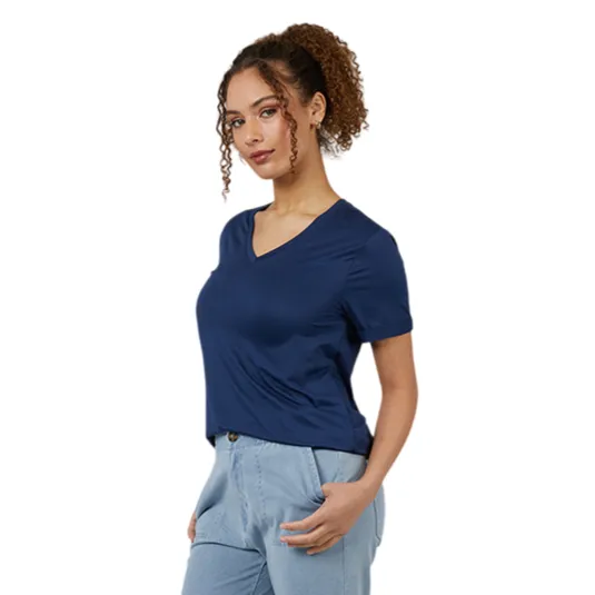 A person is wearing a navy V-neck t-shirt, light blue jeans, and blue slip-on shoes with white soles, standing against a gray background.