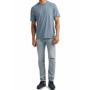 AG Dylan Slim Jeans are light-wash denim with a slim fit and feature subtle distressing, including holes near the knees. They are paired with black sneakers and a gray T-shirt.