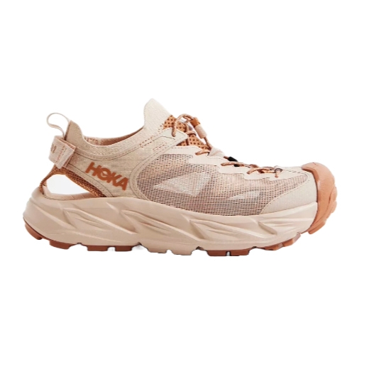 Hoka Women's Hiking Shoes in beige feature a mesh upper, open-back design, chunky sole, and prominent toe guard, offering both style and functionality for trail experiences.
