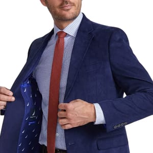 A man is wearing a Nautica Corduroy Sport Coat in navy, which features a tailored fit with a notched lapel, single breast pocket, and a patterned interior lining. He pairs it with a patterned dress shirt and a red tie.