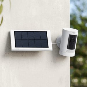 A Ring video doorbell next to its solar panel charger mounted on a wall.