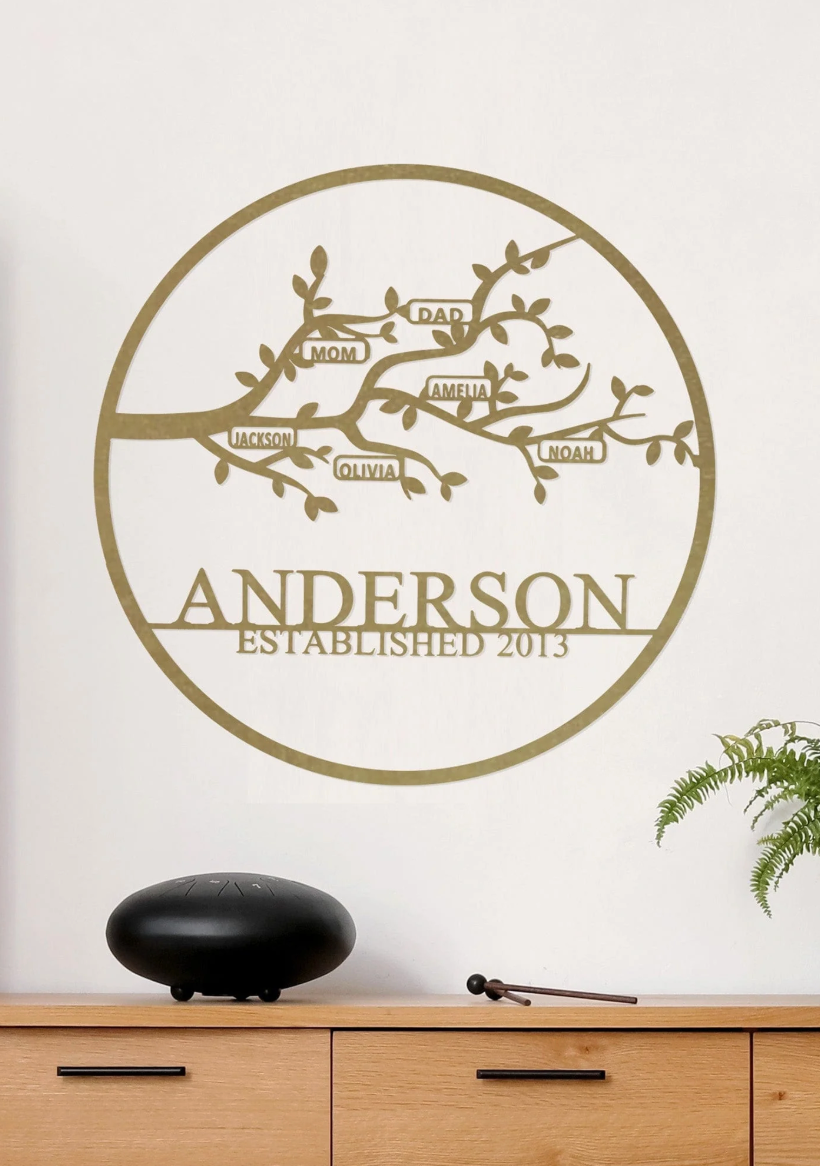 A personalized metal wall art piece features a family tree design with names \“Mom,\“ \“Dad,\“ \“Amelia,\“ \“Jackson,\“ \“Olivia,\“ and \“Noah,\“ and the text \“ANDERSON ESTABLISHED 2013.\“ It's displayed above a wooden console with a decorative black object and a plant.