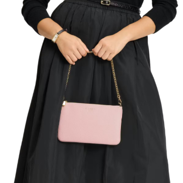 A person holds a Kate Spade Taylor wristlet with a pink leather body and gold chain strap, paired with a black skirt and sweater.
