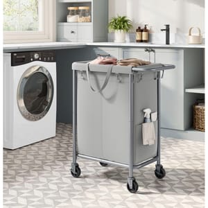 A front-loading washing machine and a grey laundry cart with clothes on casters in a kitchen.