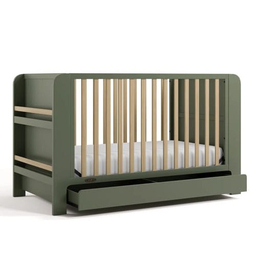 A green baby crib with natural wood slats, featuring a side storage shelf and a pull-out drawer at the bottom.
