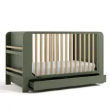 A green baby crib with natural wood slats, featuring a side storage shelf and a pull-out drawer at the bottom.