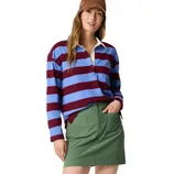 A woman wearing a striped rugby shirt in maroon and blue, paired with a green skirt featuring front pockets and a brown cap.
