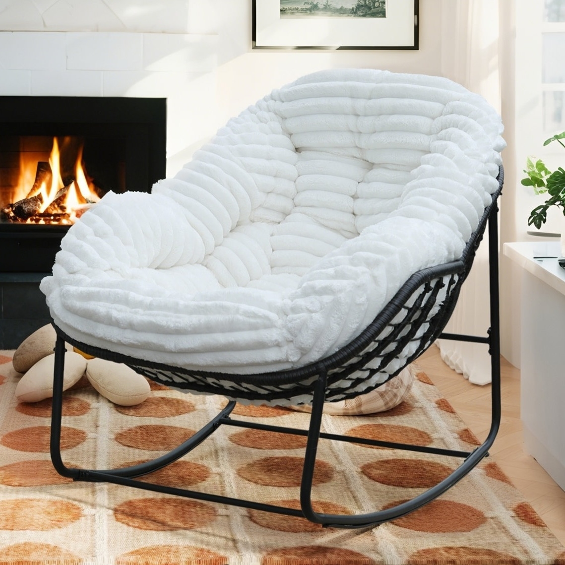 A plush, white rocking chair with a textured cushion sits on a patterned rug in front of a lit fireplace, creating a cozy atmosphere.