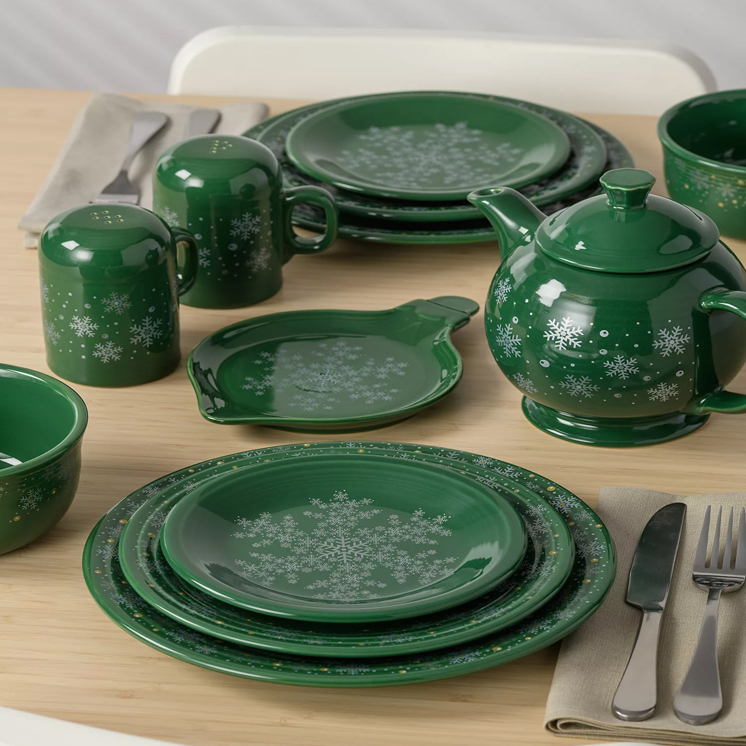 Green dinnerware set with snowflake patterns, including plates, a teapot, salt and pepper shakers, a bowl, and a sauce dish.