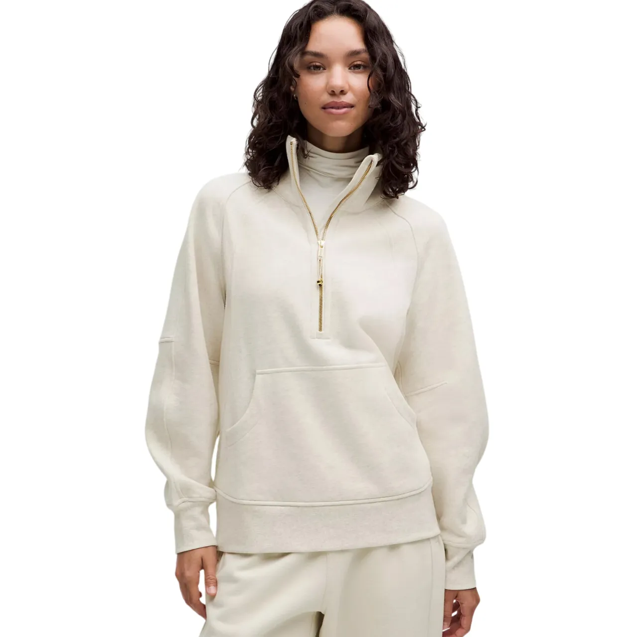 Woman wearing a cream-colored pullover with a half-zip closure, high collar, and front kangaroo pocket, paired with matching pants.