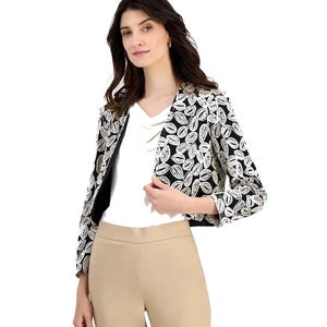 A woman is wearing a black and white leaf-patterned jacket over a white top, paired with beige trousers.