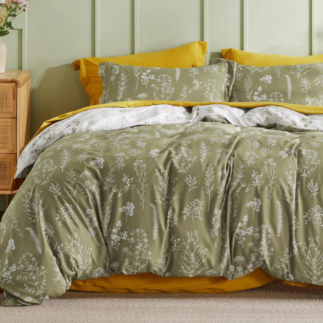 A bedding set with a botanical design features olive green sheets and a duvet cover, adorned with white floral patterns. The set is complemented by mustard yellow pillowcases and an underlayer.