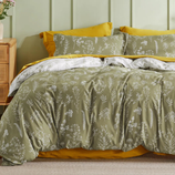 A bedding set with a botanical design features olive green sheets and a duvet cover, adorned with white floral patterns. The set is complemented by mustard yellow pillowcases and an underlayer.