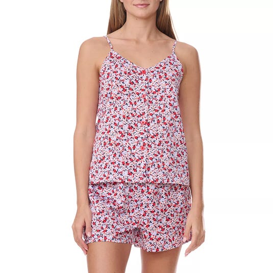 A woman is wearing a floral print pajama set featuring a sleeveless camisole top with thin straps and matching shorts. The pattern includes red, black, and white flowers.