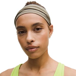 A person wearing a beige headband and a light green tank top with small hoop earrings.