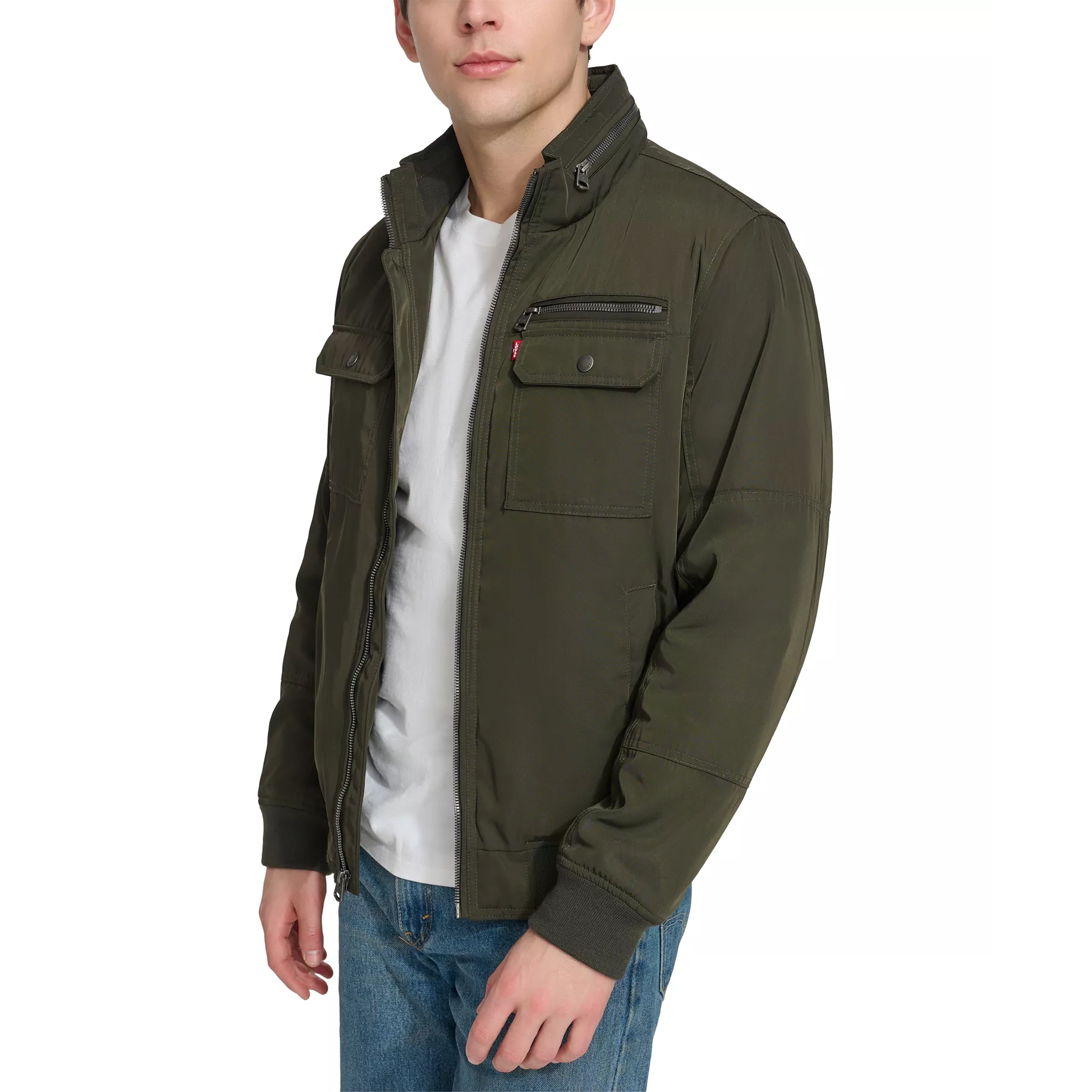 A man is wearing an olive green jacket with multiple pockets, paired with a white T-shirt and blue jeans.