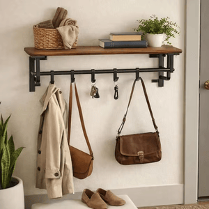 A wall-mounted shelf and hook rack features a wooden shelf holding books and a plant, and hooks below holding a coat, handbags, and keys. Beneath it sits a pair of shoes.