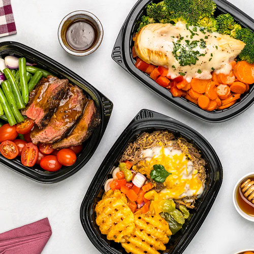 Three meal containers feature dishes: grilled steak with green beans and tomatoes, chicken breast over broccoli and carrots, and a dish with cheesy rice, vegetables, and waffle fries. Sauces in small cups are also included.