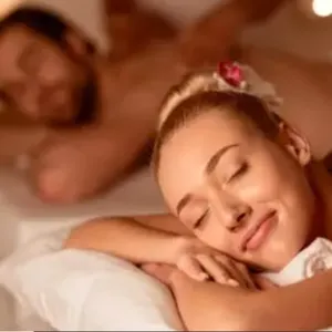 A woman and a man are receiving massages in a dimly lit, relaxing setting, lying on massage tables with candles in the background.