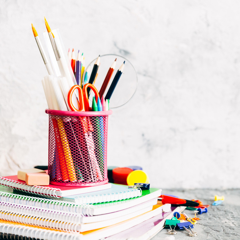 A selection of stationery including colored pencils, pens, notebooks, and scissors on a white background.