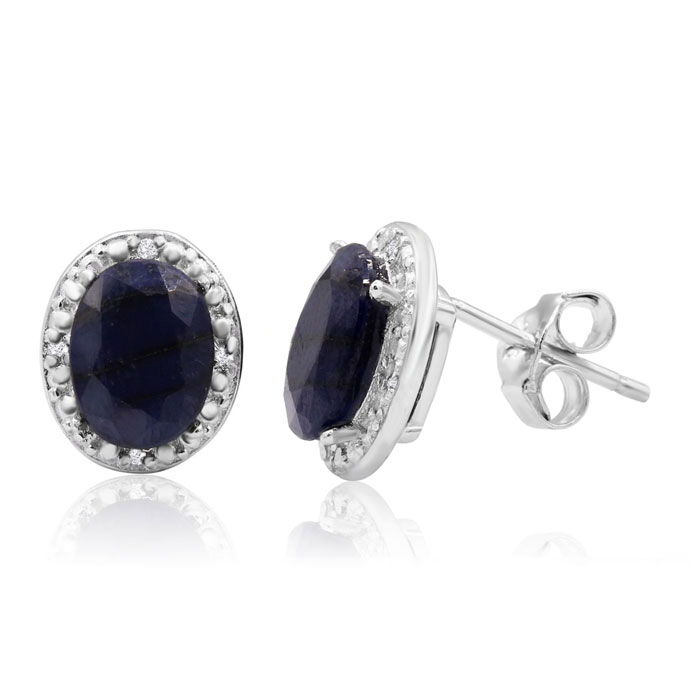 Oval-shaped sapphire and diamond stud earrings feature a deep blue sapphire center encircled by small round diamonds set in a white metal, with traditional stud backs.