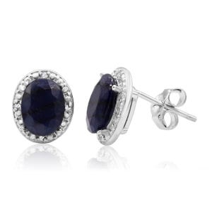 Oval-shaped sapphire and diamond stud earrings feature a deep blue sapphire center encircled by small round diamonds set in a white metal, with traditional stud backs.