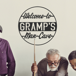 A sign reads \“Welcome to Gramp's Man-Cave\“ with a playful vintage style. Three elderly men are engaged in a pool game beneath the sign.