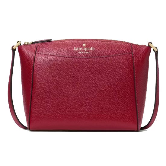 A red leather crossbody bag with a subtle pebbled texture, featuring a zippered top and thin adjustable strap, labeled \“kate spade new york\“ on the front.