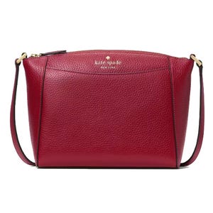 A red leather crossbody bag with a subtle pebbled texture, featuring a zippered top and thin adjustable strap, labeled \“kate spade new york\“ on the front.