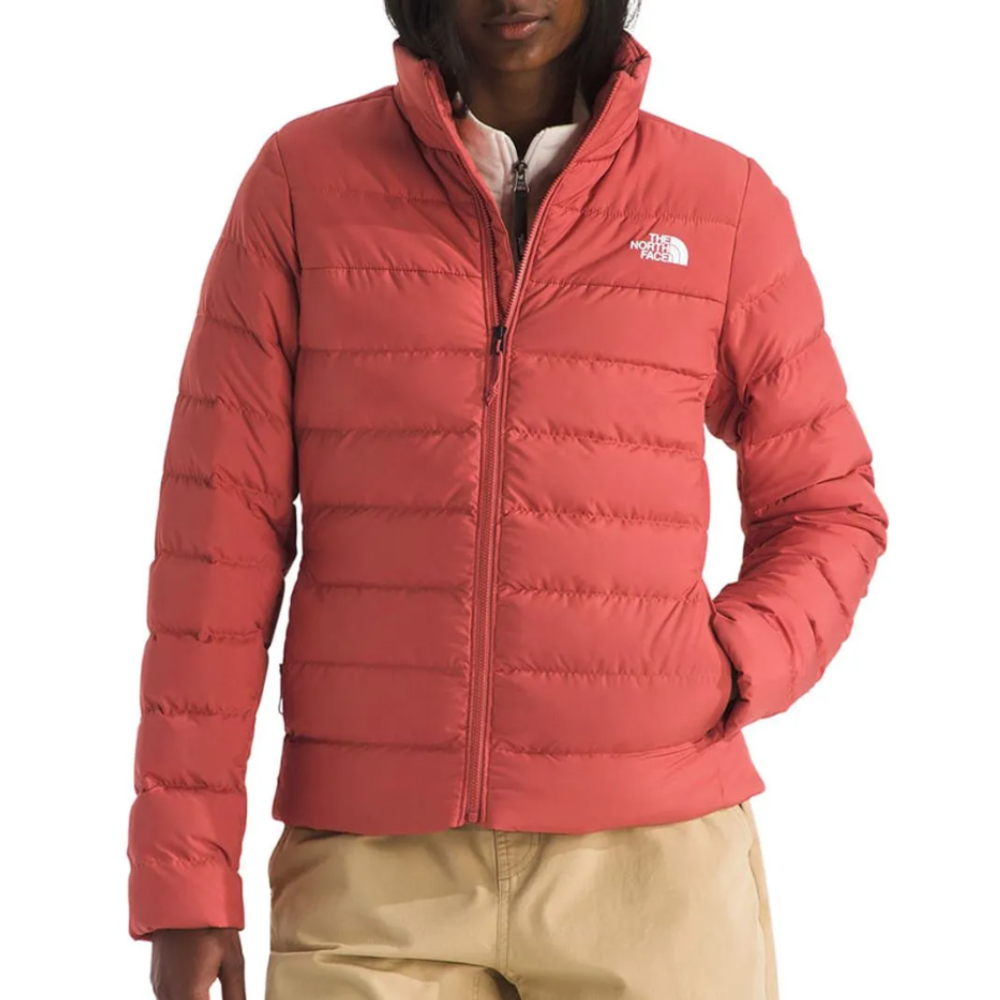 A red The North Face puffer jacket with a zip-up front and logo on the chest, worn by a person in beige pants.