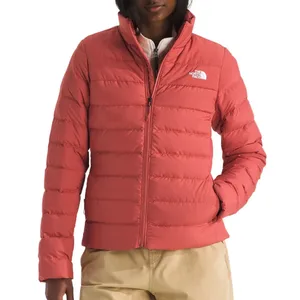 A red The North Face puffer jacket with a zip-up front and logo on the chest, worn by a person in beige pants.