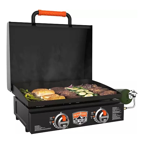 A portable Blackstone 22-inch griddle featuring two burners, a rear grease management system, and a foldable black hood on top, with food items cooking on the surface.