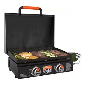 A portable Blackstone 22-inch griddle featuring two burners, a rear grease management system, and a foldable black hood on top, with food items cooking on the surface.