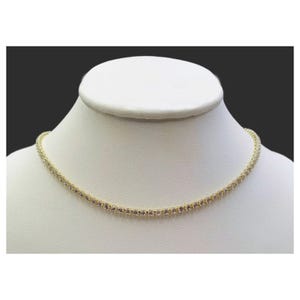 Gold-tone necklace with embedded clear gemstones displayed on a white bust form.